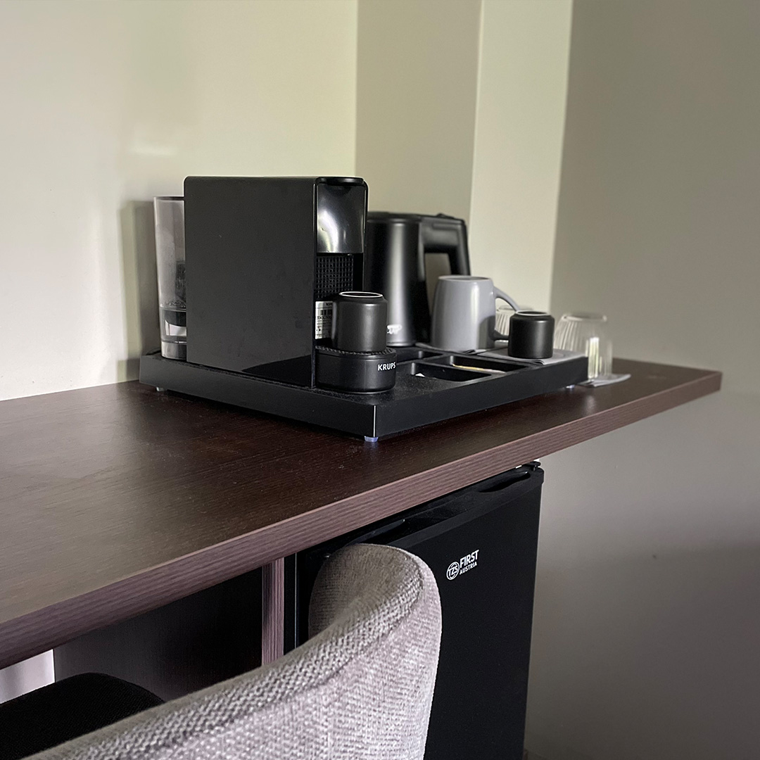 Kaffeemaschine steht auf Holzablage im Zimmer, daneben Tassen und Wasserkocher